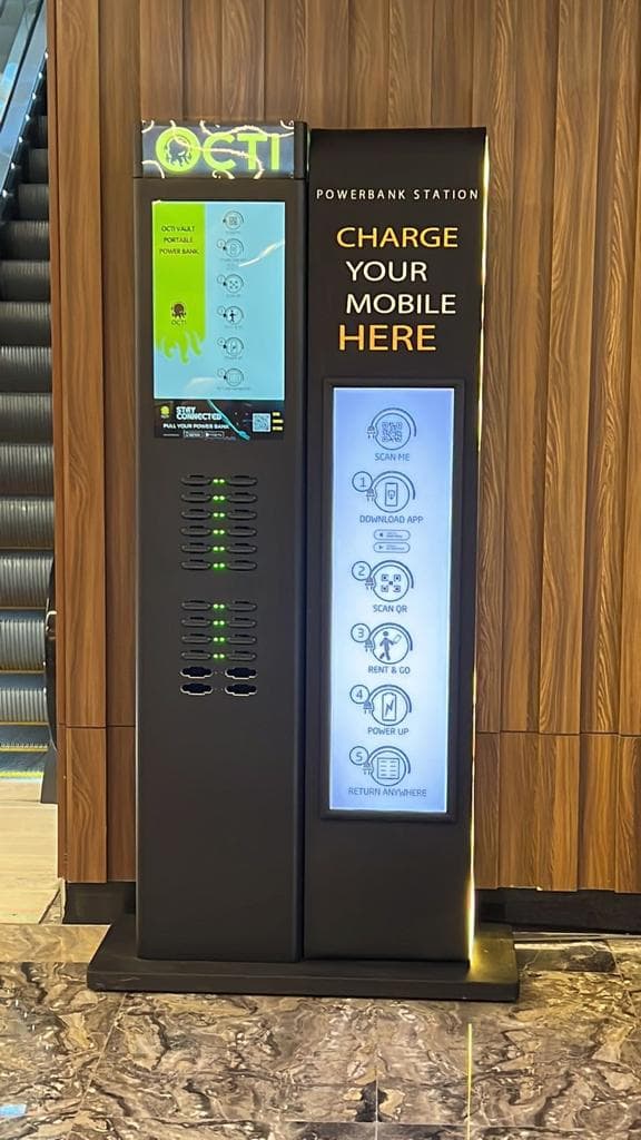A charging station installed beside an escalator, its screen showing rental instructions