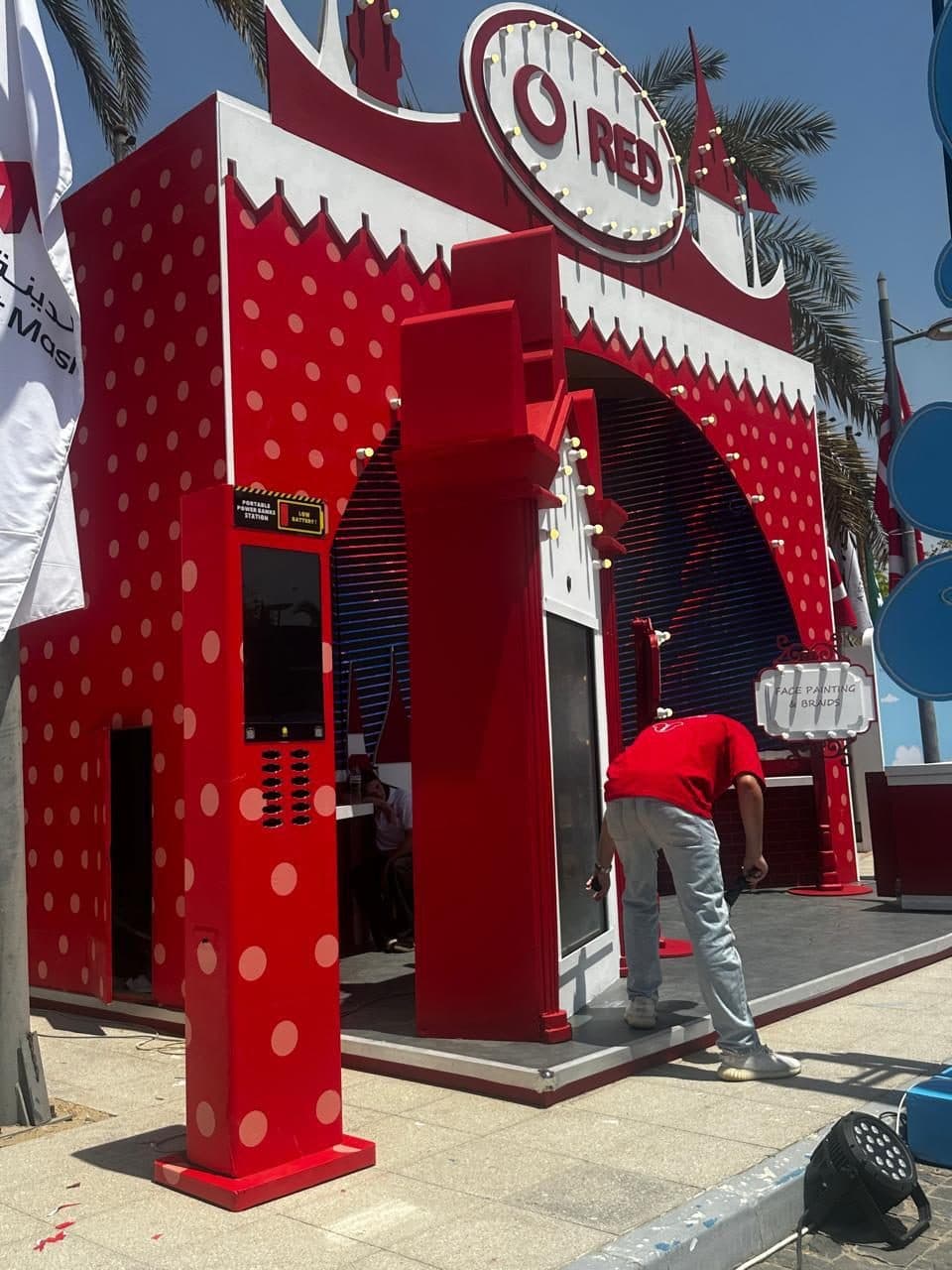 A red polka-dot charging station beside a matching carnival-style event booth under construction