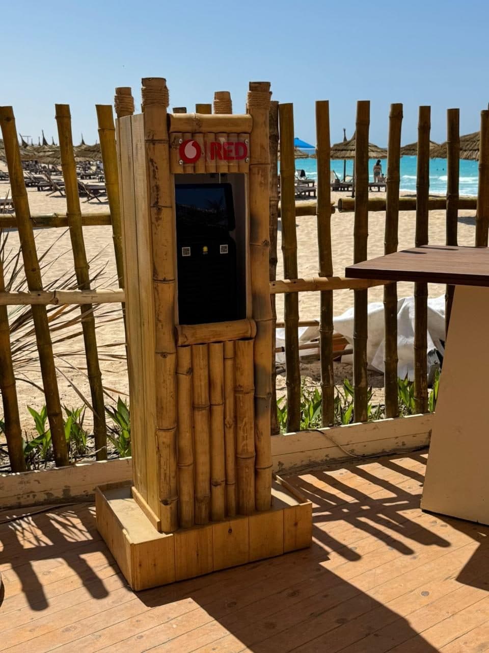 A bamboo-clad charging station on a wooden deck, with sun loungers and open sea behind it